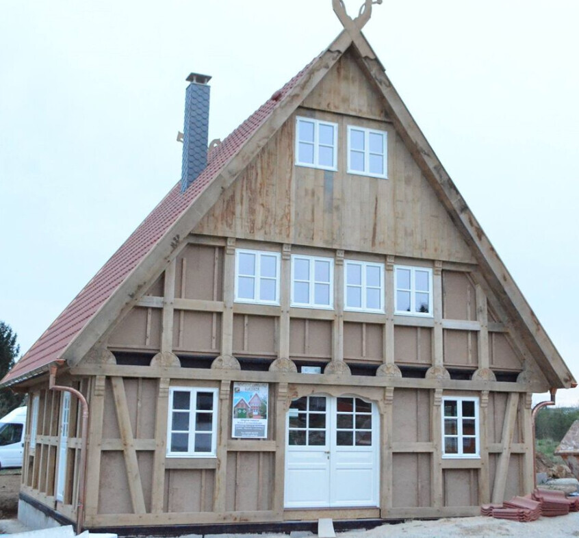 Fachwerkhaus im Bau mit rotem Satteldach, weißen Fenstern und Türen, sichtbare Holzbalken