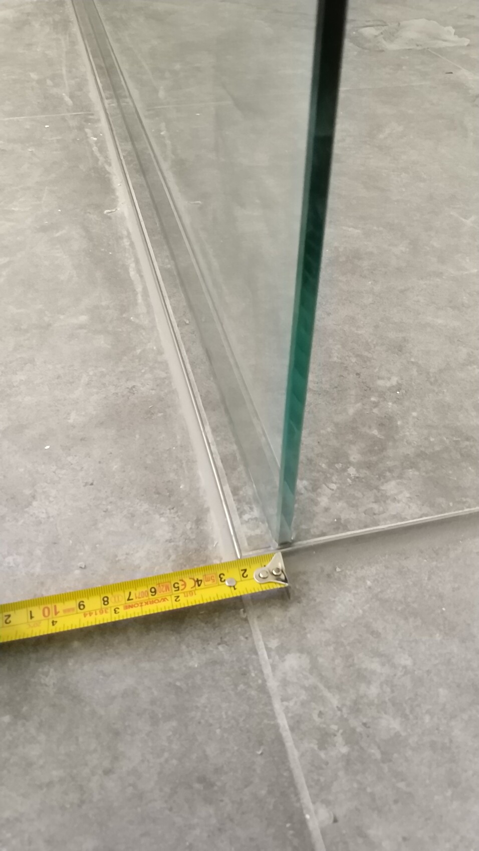 Nahaufnahme einer Glaswand mit gelbem Messband am Boden, grünem Glasrand.