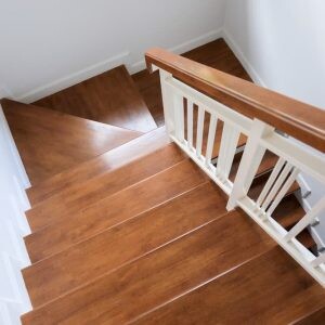 Innenaufnahme einer Holztreppe mit braunen Stufen und weißem Geländer von oben