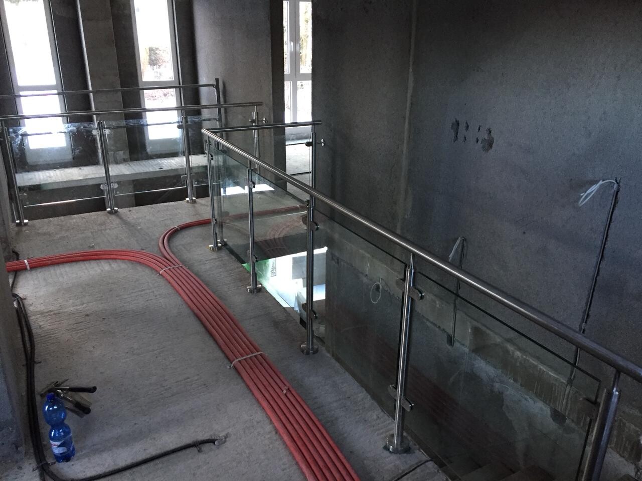 Innenraum einer Baustelle: Glasgeländer, rote Kabelrohre auf dem Boden, offener Blick nach unten.