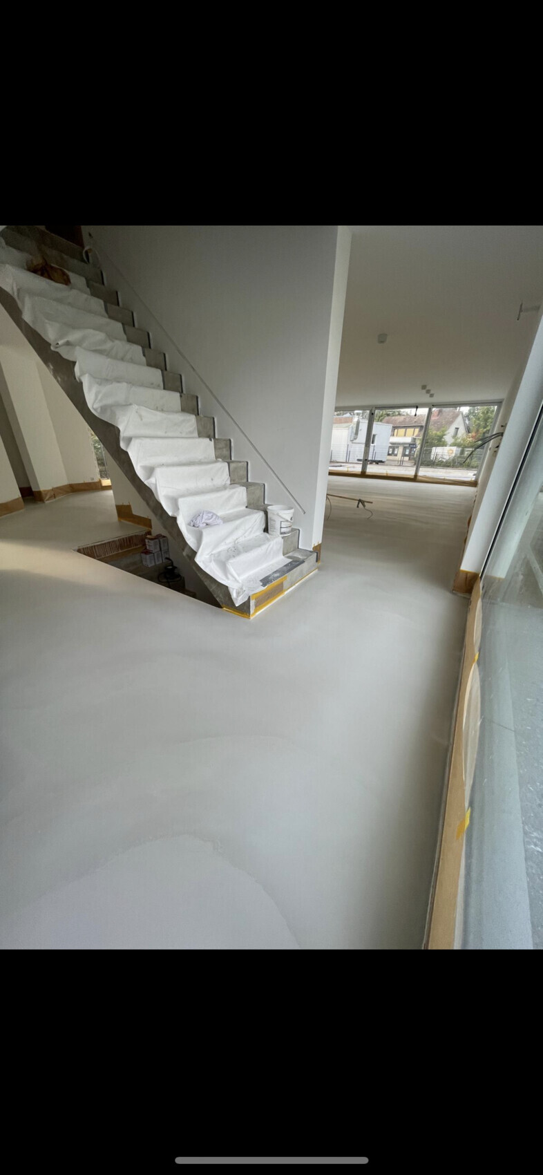 Heller Innenraum im Bau: Treppe mit Abdeckung, große Fensterfront, glatter Boden.
