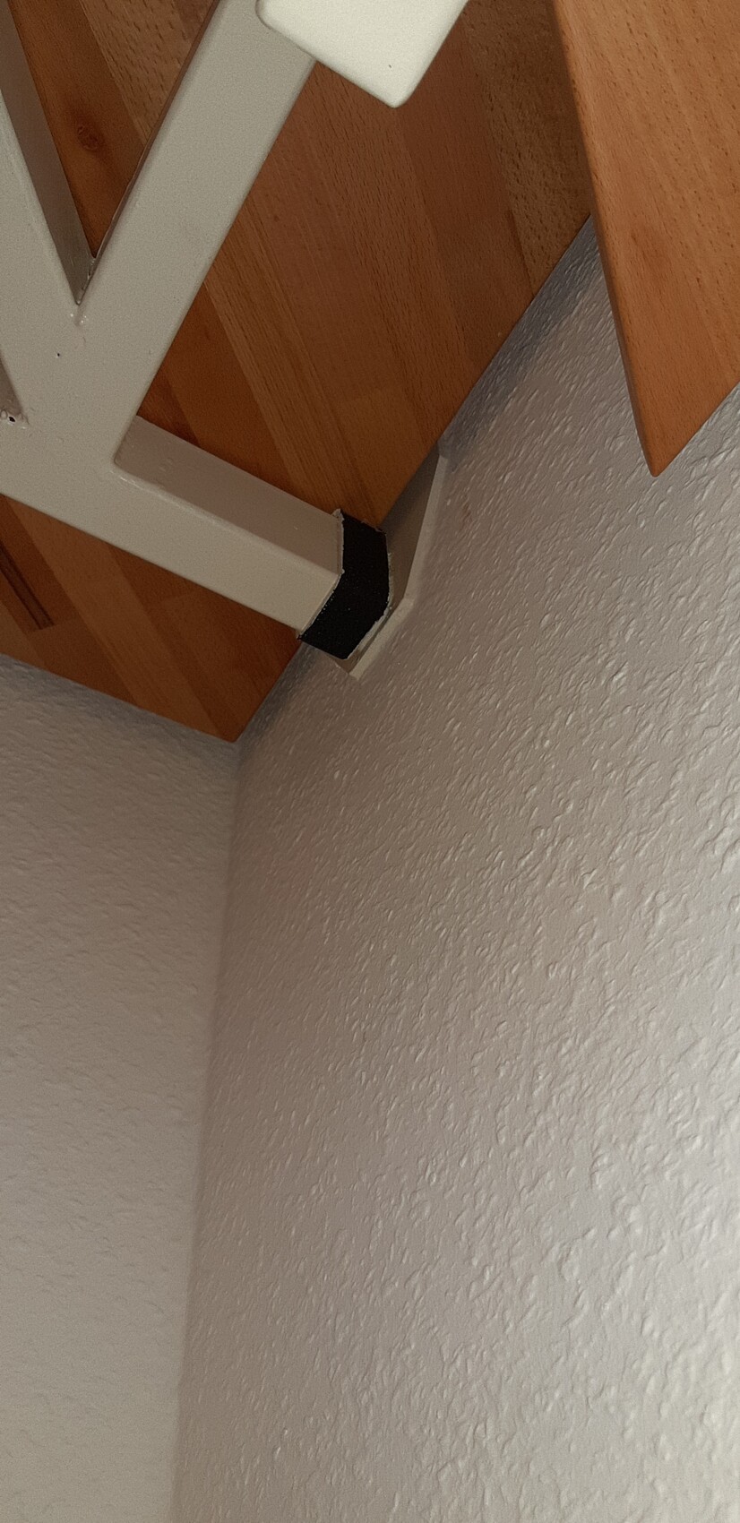 Weißer Metallträger an der Wand unter einer Holzbalkendecke; Ecke mit schwarzer Schutzkappe.