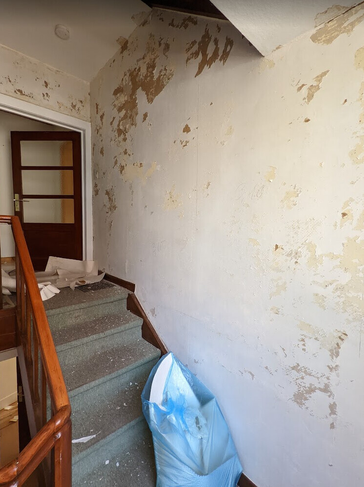Treppenhaus mit abblätternder Wand, Treppenstufen und blauem Müllsack.