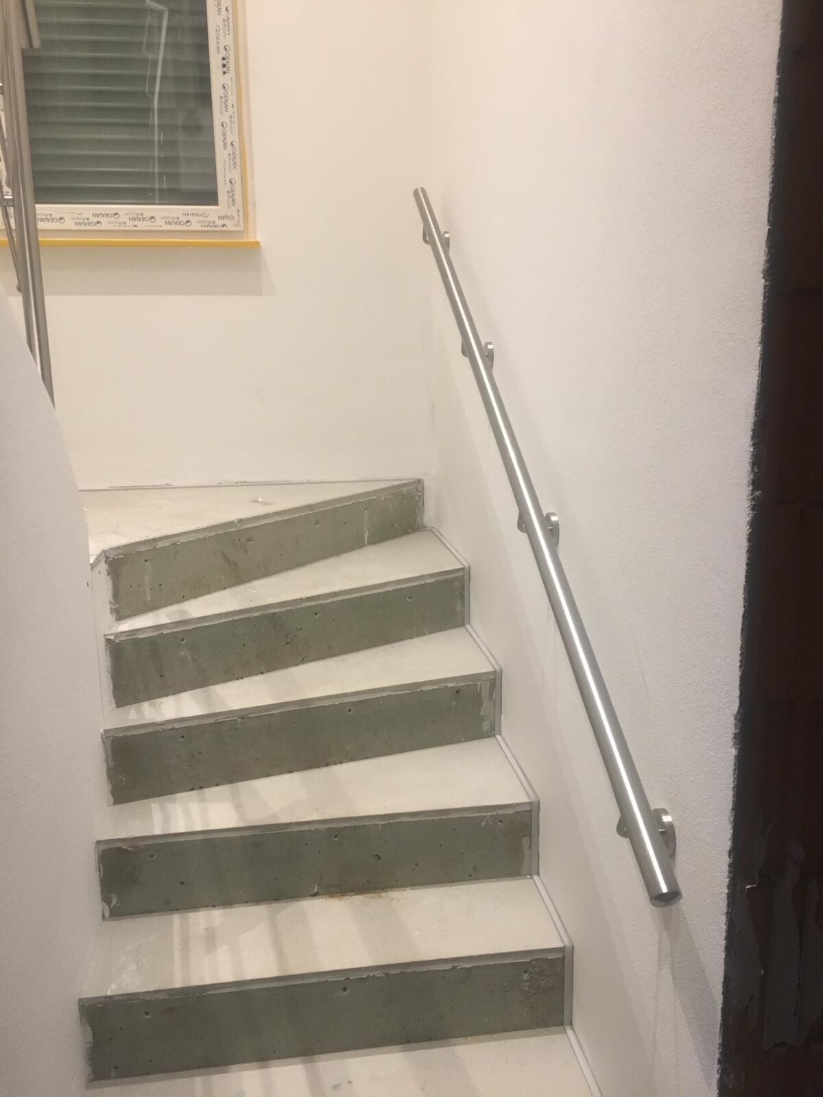 Innenstiege: weiße Wände, Betonstufen, silbernes Geländer rechts.