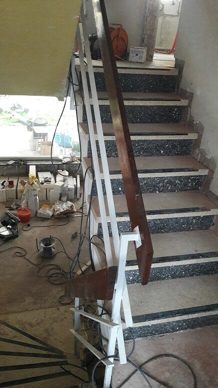 Baustelle im Innenbereich mit Treppe, Holzhandlauf und Baumaterialien.
