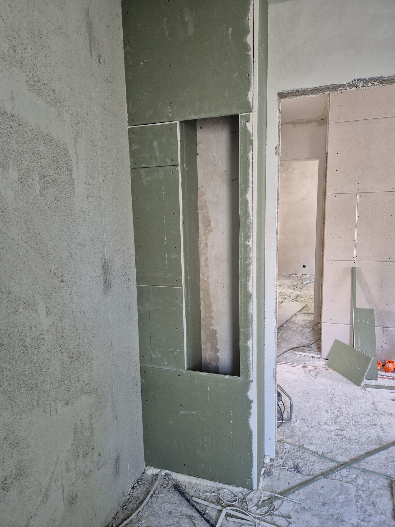 Baustelle: grüne Trockenbauwand mit Nische, unfertige Innenräume und verstreute Platten.