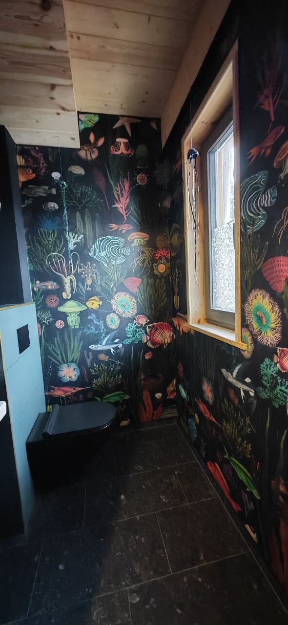 Badezimmer mit farbigem Unterwasser-Wandtattoo, Fenster, Toilette und dunklen Fliesen.