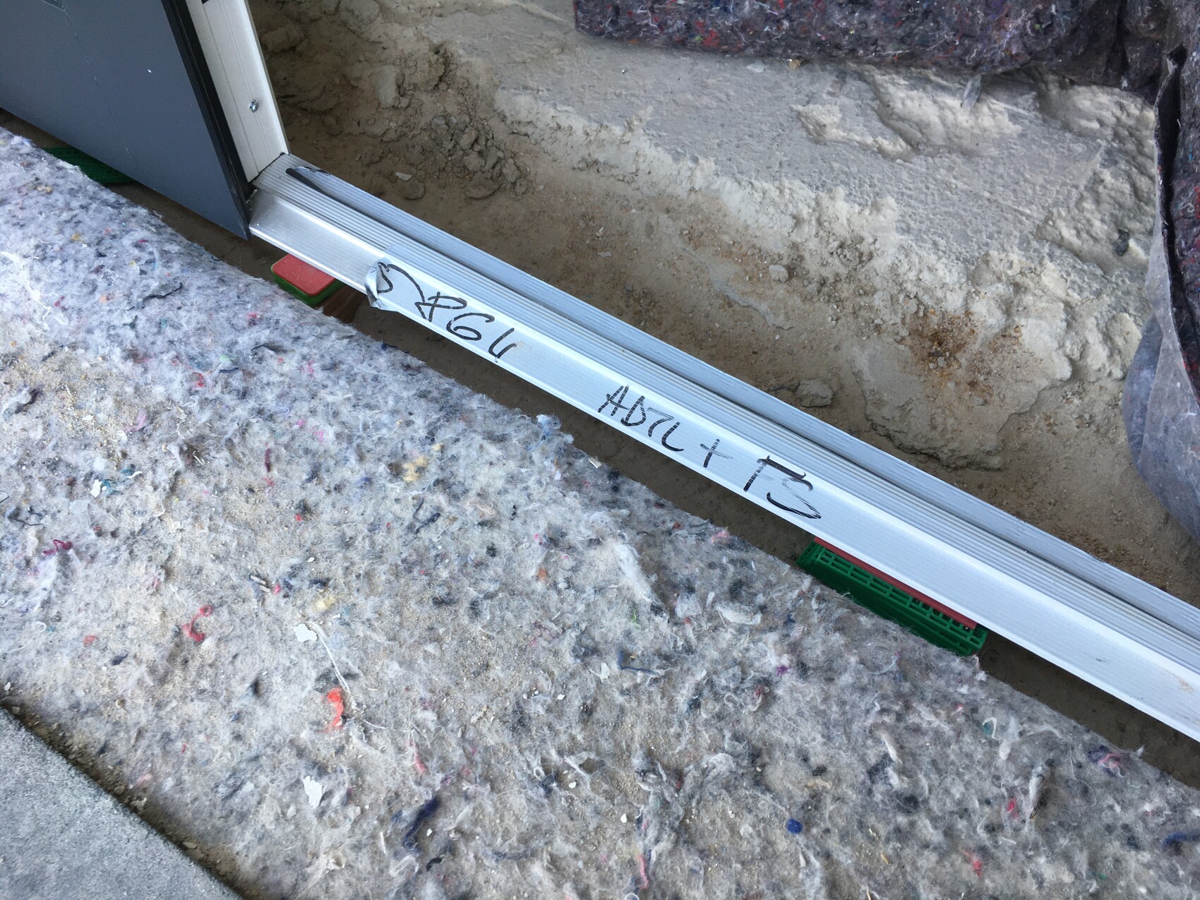 Metall-Schiebetürführung liegt auf staubigem Baugrund neben offenem Türrahmen.