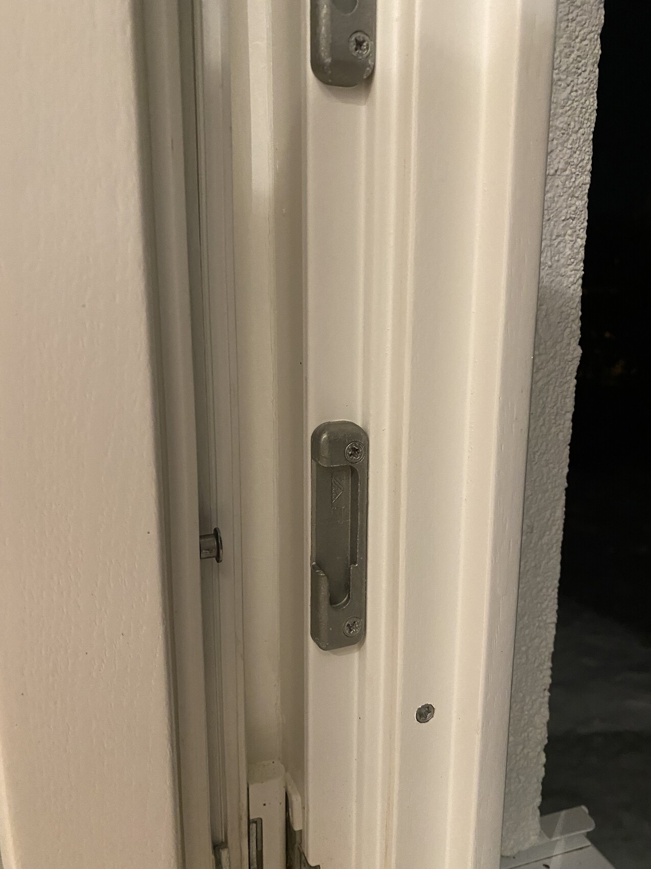 Nahaufnahme eines weißen Türrahmens mit Metall-Schlossstossplatte und Schrauben.