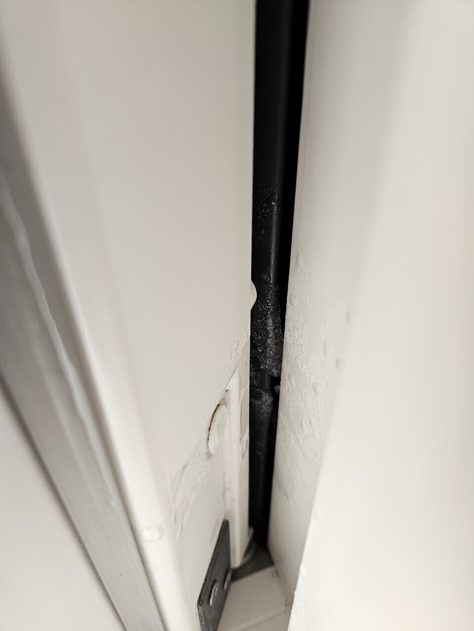 Nahaufnahme eines engen Spalts zwischen zwei weißen Flächen; schwarze Stange dazwischen.