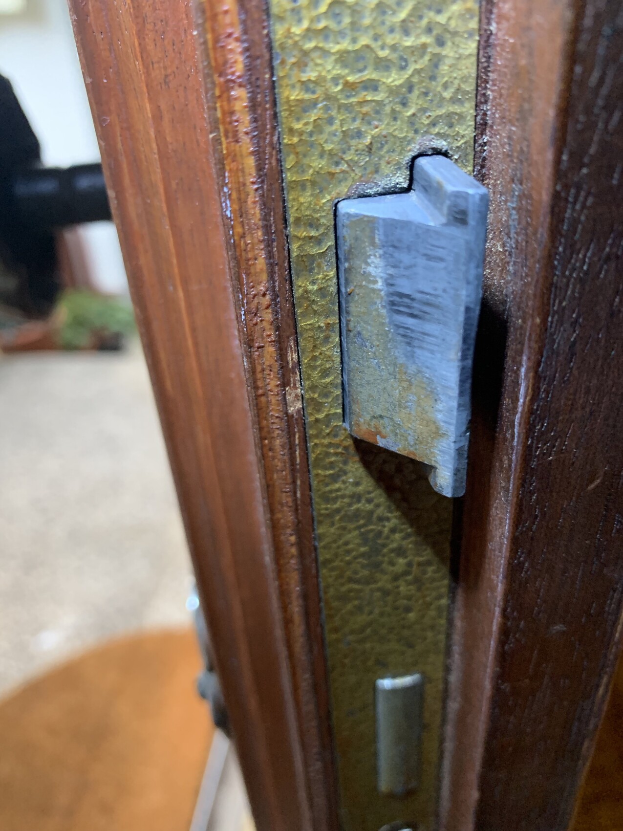 Nahaufnahme eines korrodierten Türbeschlags am Türrahmen mit metallischer Platte.