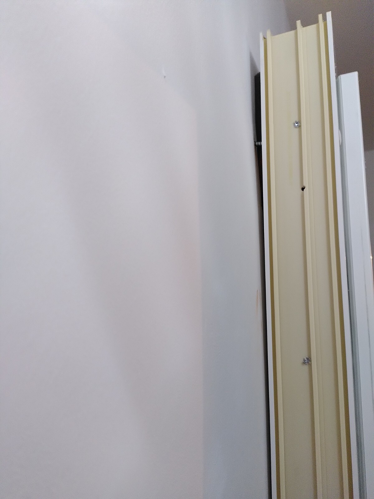 Beige Türrahmen-Leisten stehen dicht an einer weißen Wand, Schrauben sichtbar.