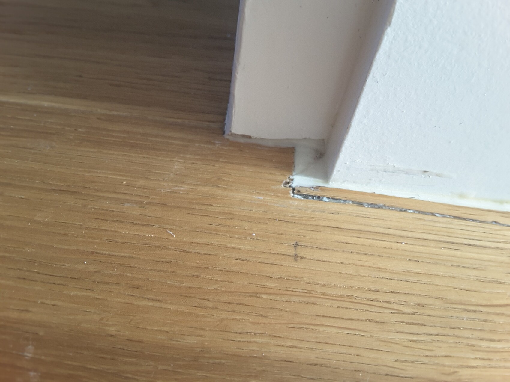 Nahaufnahme eines weißen Türrahmens am Holzboden mit Spalt zwischen Boden und Rahmen.