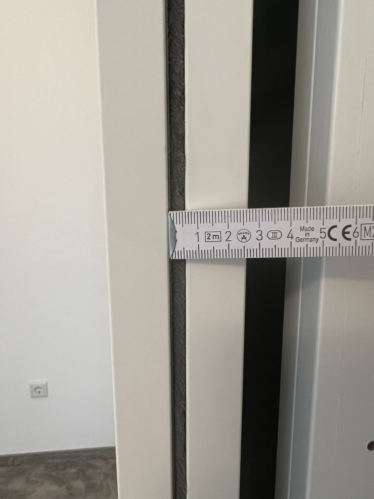 Nahaufnahme eines Maßbands, das einen Spalt zwischen weißen Türrahmen zeigt.