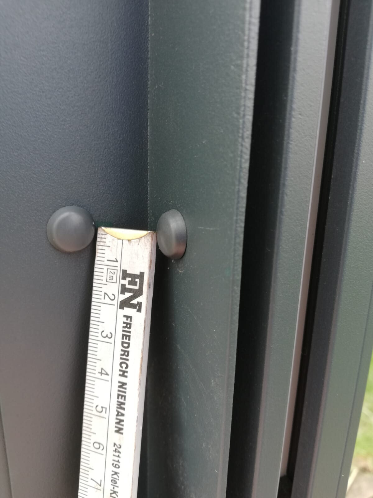 Messband misst Spalt am grünem Türrahmen mit runden Gummipuffern.
