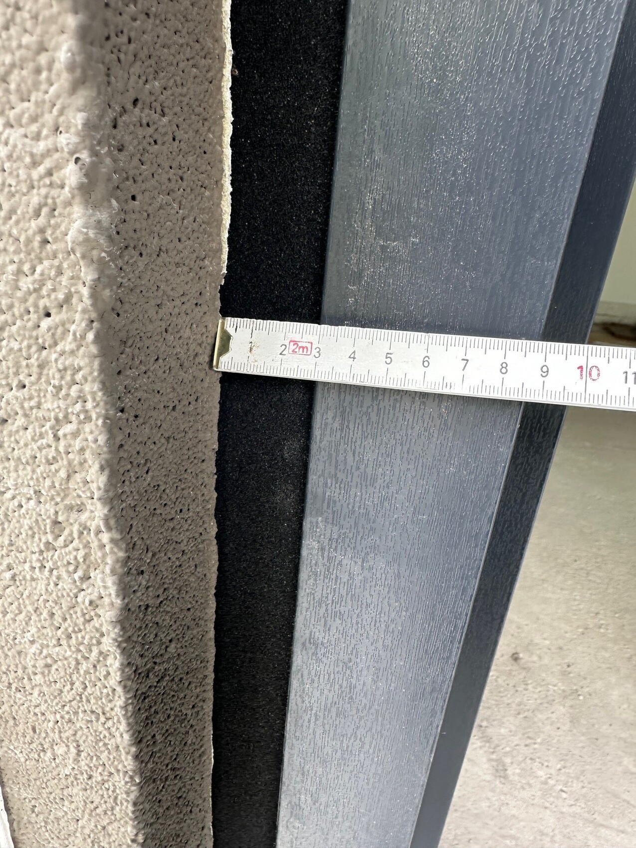 Nahaufnahme eines Maßbands zeigt Spalt zwischen grauem Türrahmen und Putzwand
