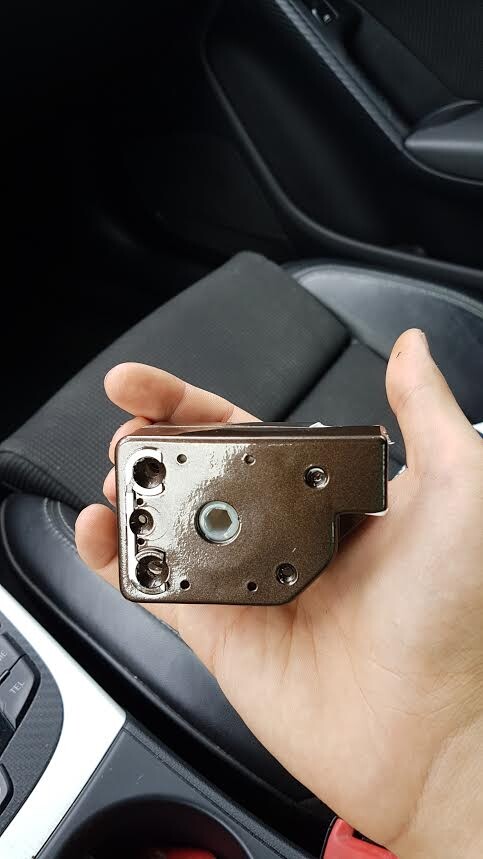 Hand hält braunes Metall-Türschloss-Bauteil im Innenraum eines Autos.