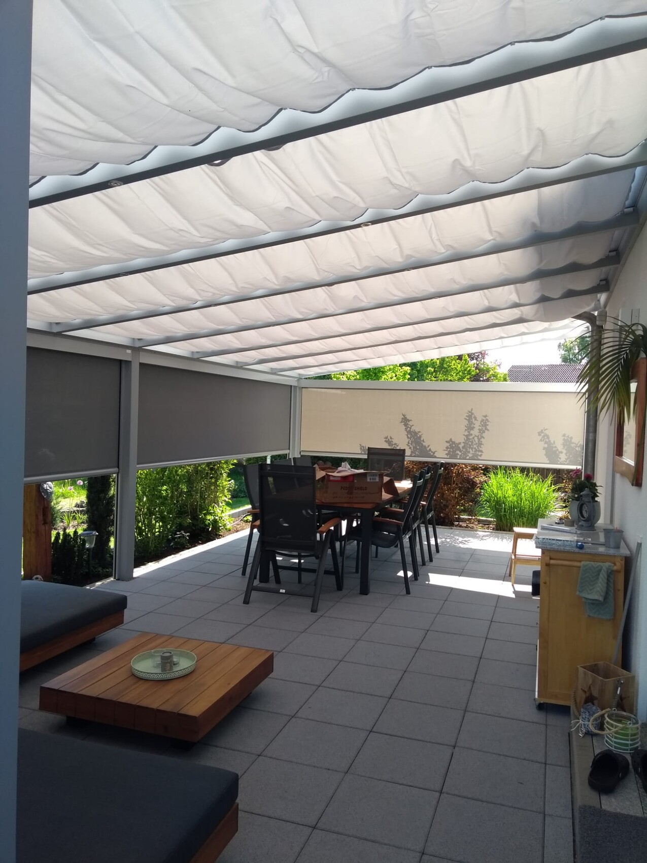 Gedeckte Terrasse mit weißem Stoffdach, Esstisch und Stühle, Lounge-Sofa und Pflanzen.