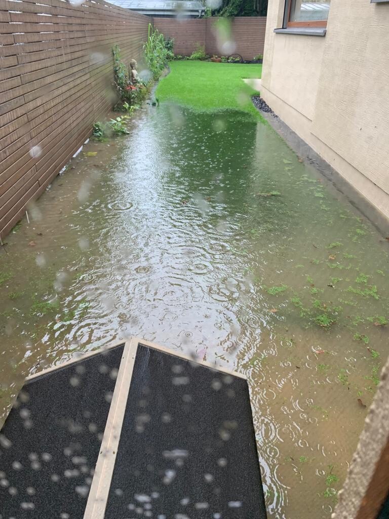 Überfluteter Garten- und Terrassenbereich neben dem Haus mit stehenden Regenpfützen