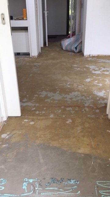 Blick in einen Flur eines Hauses; Boden stark beschädigt mit Flecken, Tür am Ende.