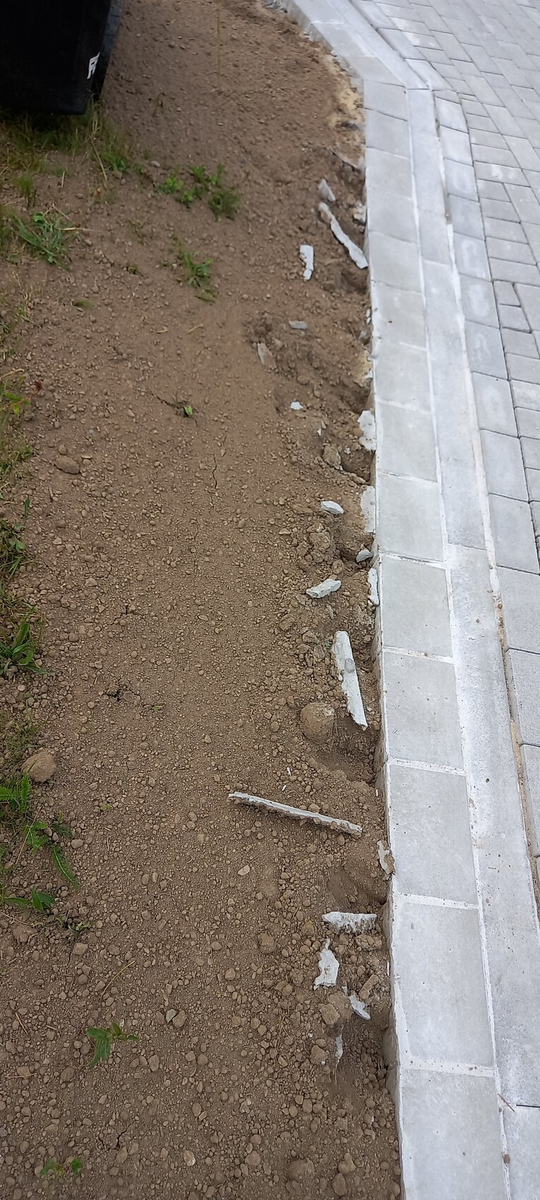 Unbefestigte Erdfläche neben Bordsteinkante mit abgebrochenen Betonstücken und Gehwegplatten