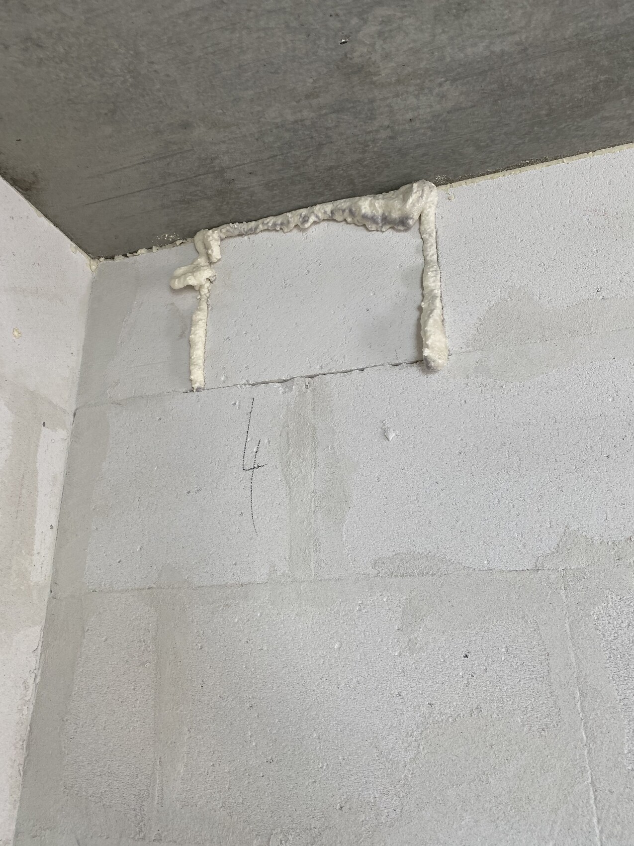 Unfertige Innenwand-Ecke; rohes Mauerwerk, weißer PU-Schaum dichtet die Deckenfuge ab.