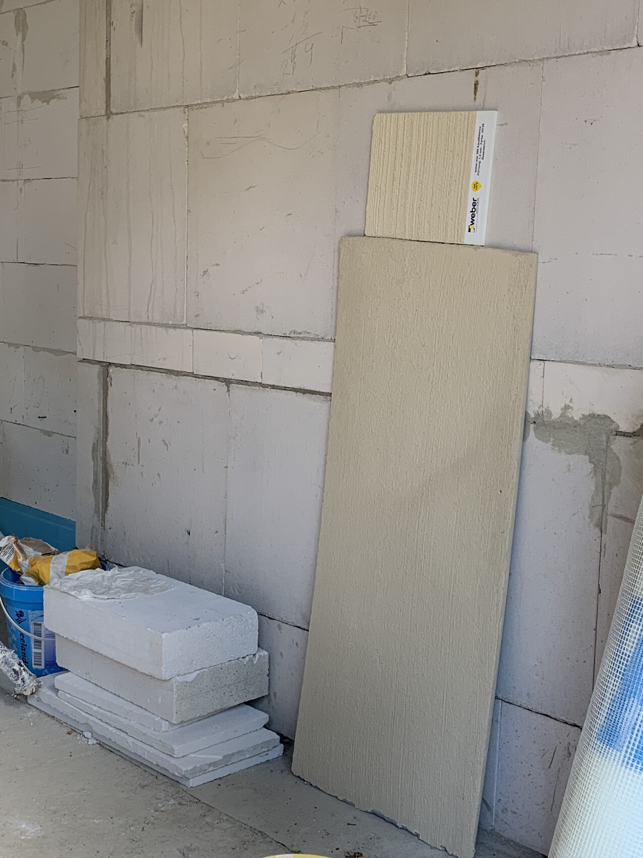 Baustelle: Große beige Dämmplatte lehnt an Betonwand; daneben Styroporplatten und Putzreste.