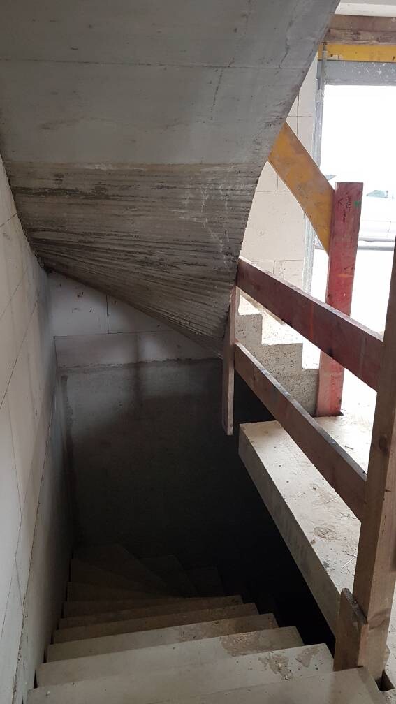 Betontreppe auf Baustelle mit Holzgeländer und dunklem Kellergeschoss.