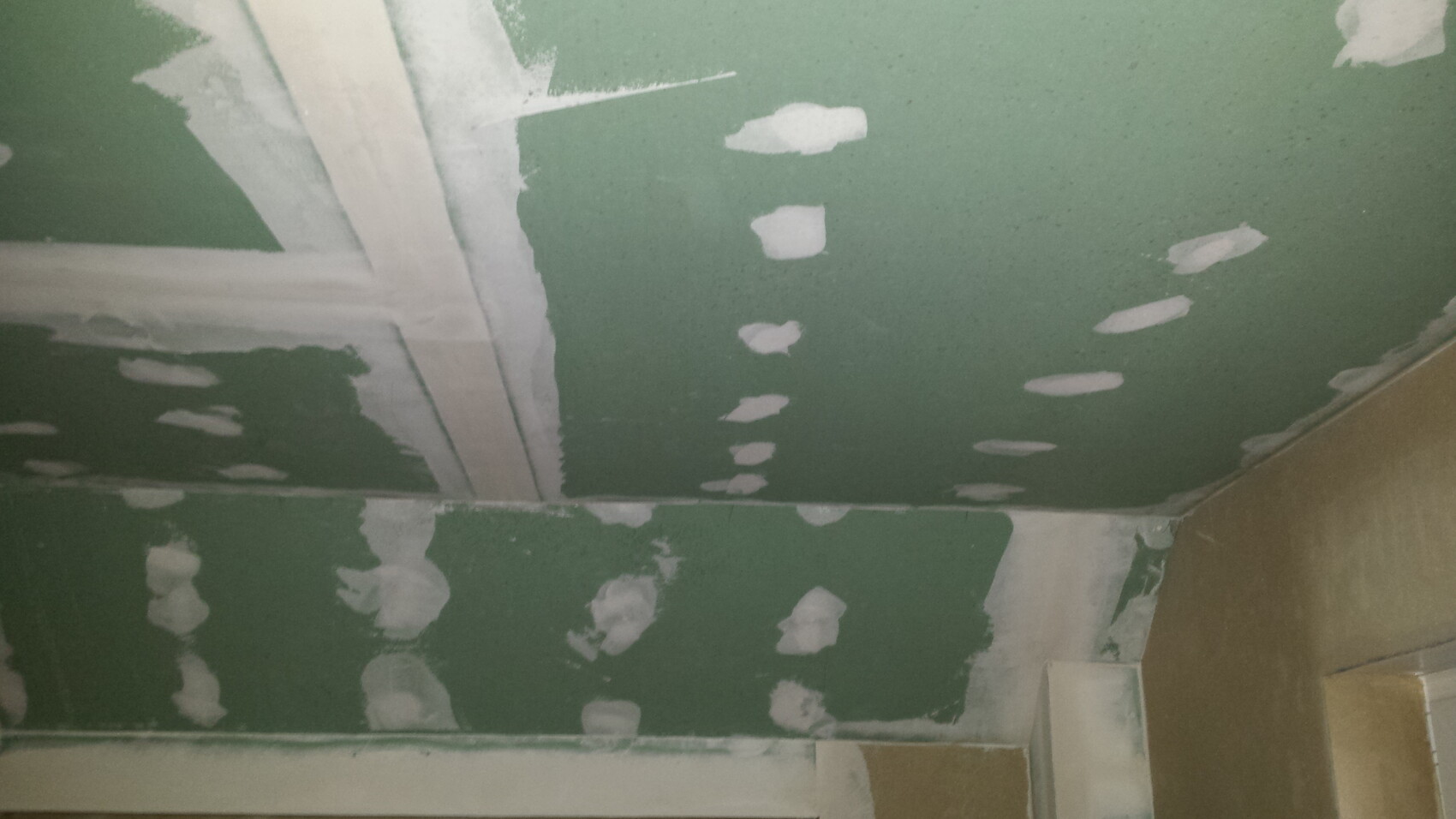 Grüne Trockenbauwand mit vielen weißen Spachtelstellen an Fugen und Ecken.