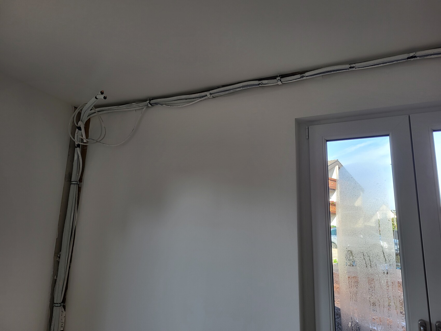 Ecke eines Zimmers mit freiliegenden Kabeln entlang der Decke und einer Glastür mit milchigem Muster