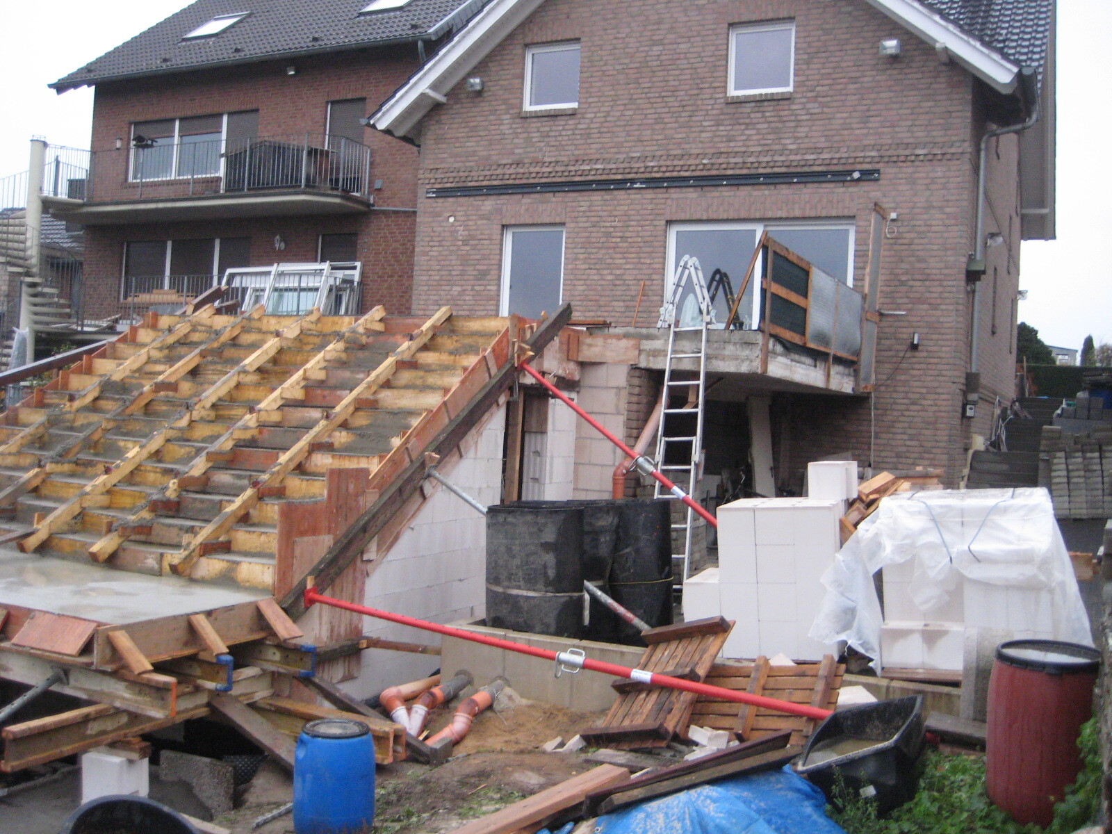 Baustelle an einem Wohnhaus mit offenem Holzdachstuhl, Leitern, Baumaterialien und Zementblöcken.