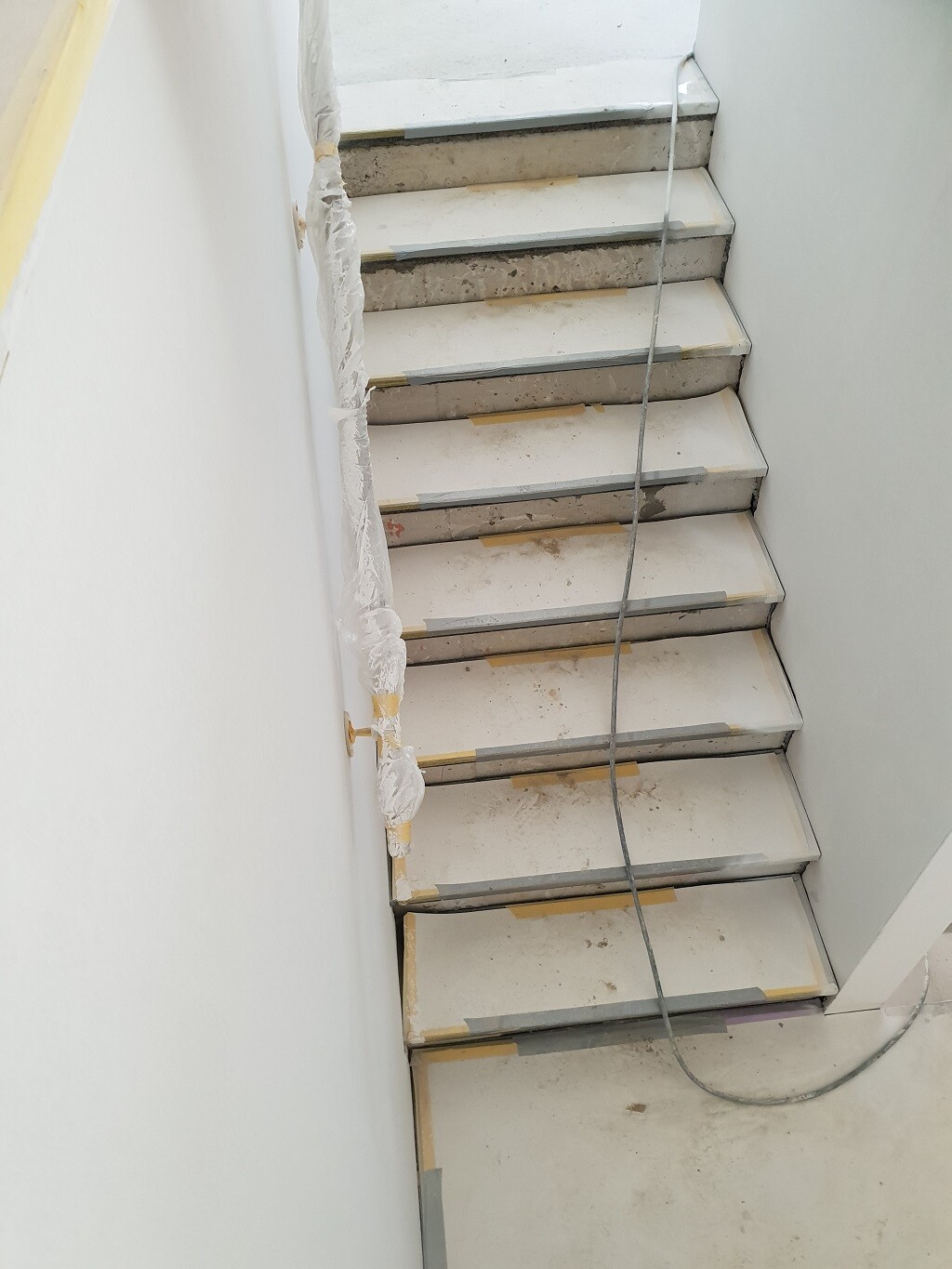 Unfertige Innen-Treppe im Bau, Staub, Kabel und Schutzfolie an der Wand