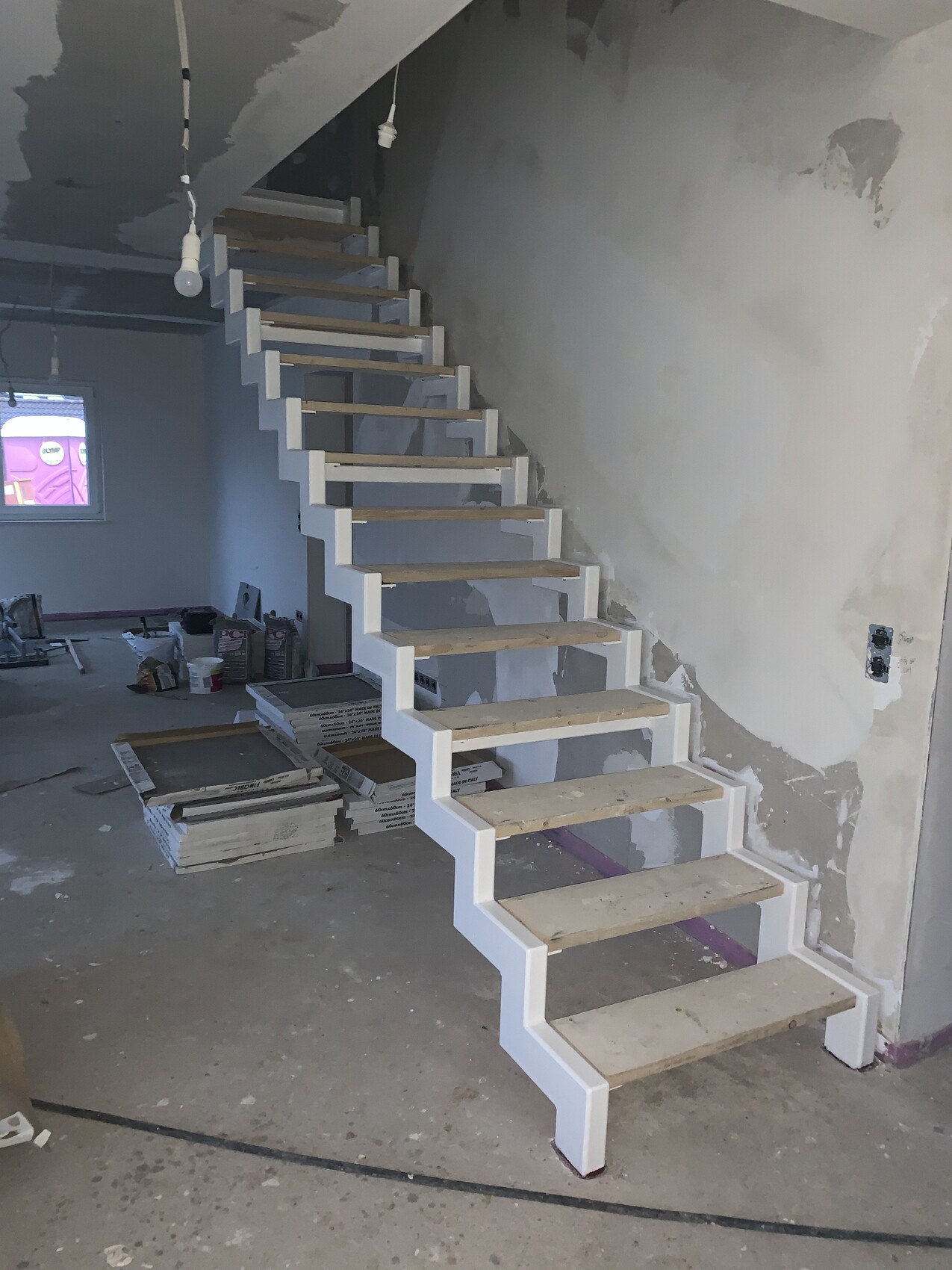 Moderne offene Treppe mit weißen Stützen und Holzdielen in unfertigem Innenraum, Bauarbeiten.