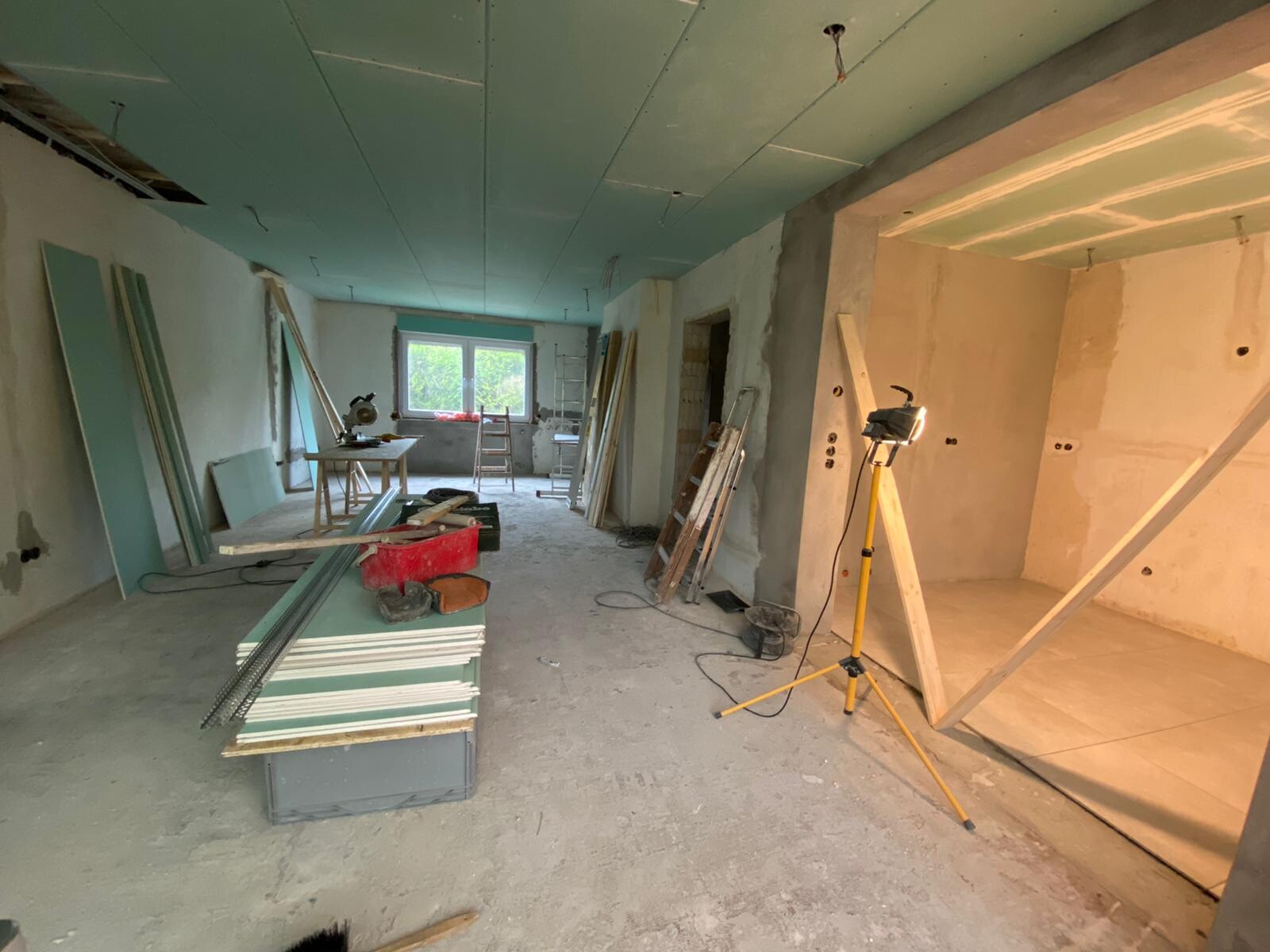 Innenraum einer Baustelle mit Brettern, Plattenstapeln, Leiter und Baustellenlicht.