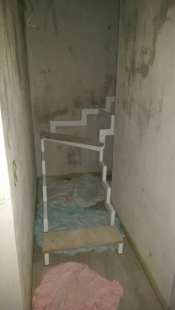 Kleiner improvisierter Treppenaufbau aus weißen Rahmen und Brettern in engem unfertigem Kellerraum.