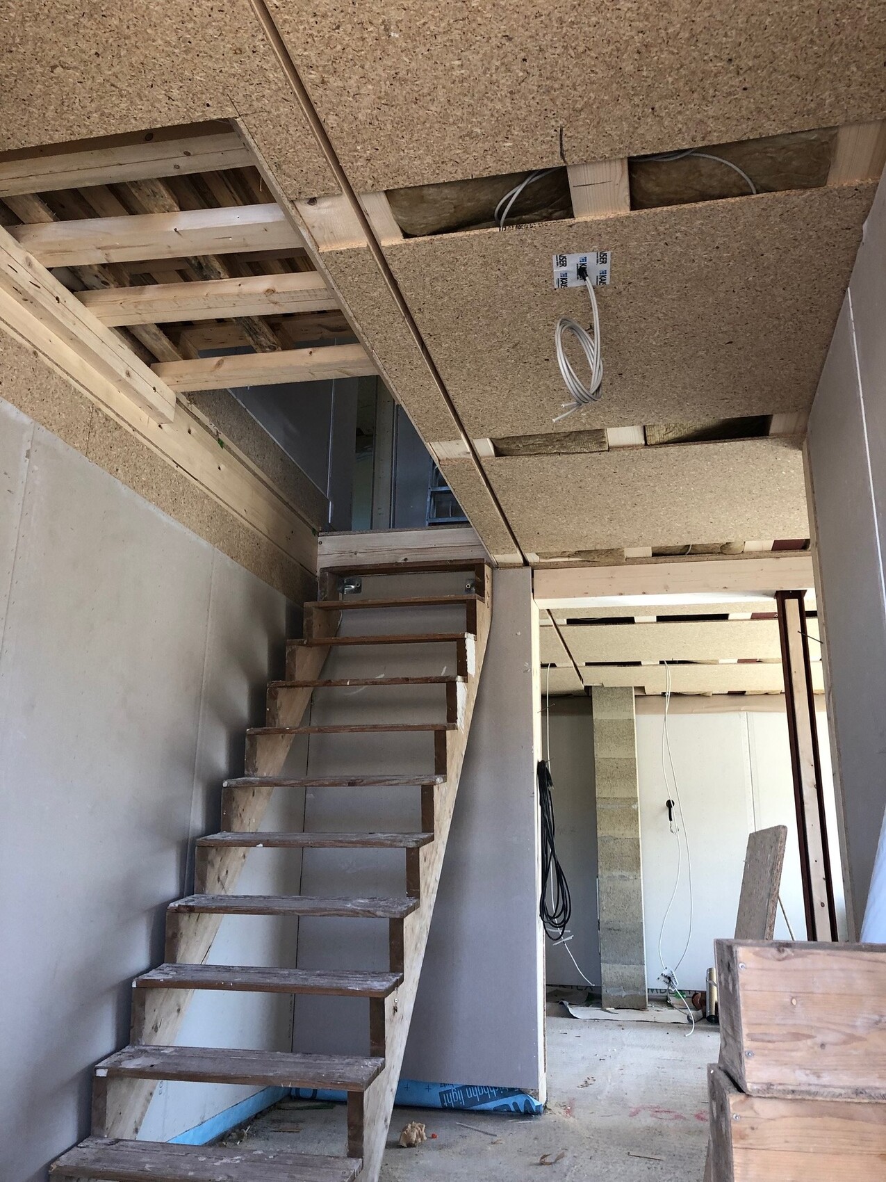 Unfertiger Innenraum mit Holztreppe, offene Decke aus OSB-Platten und Baukabeln