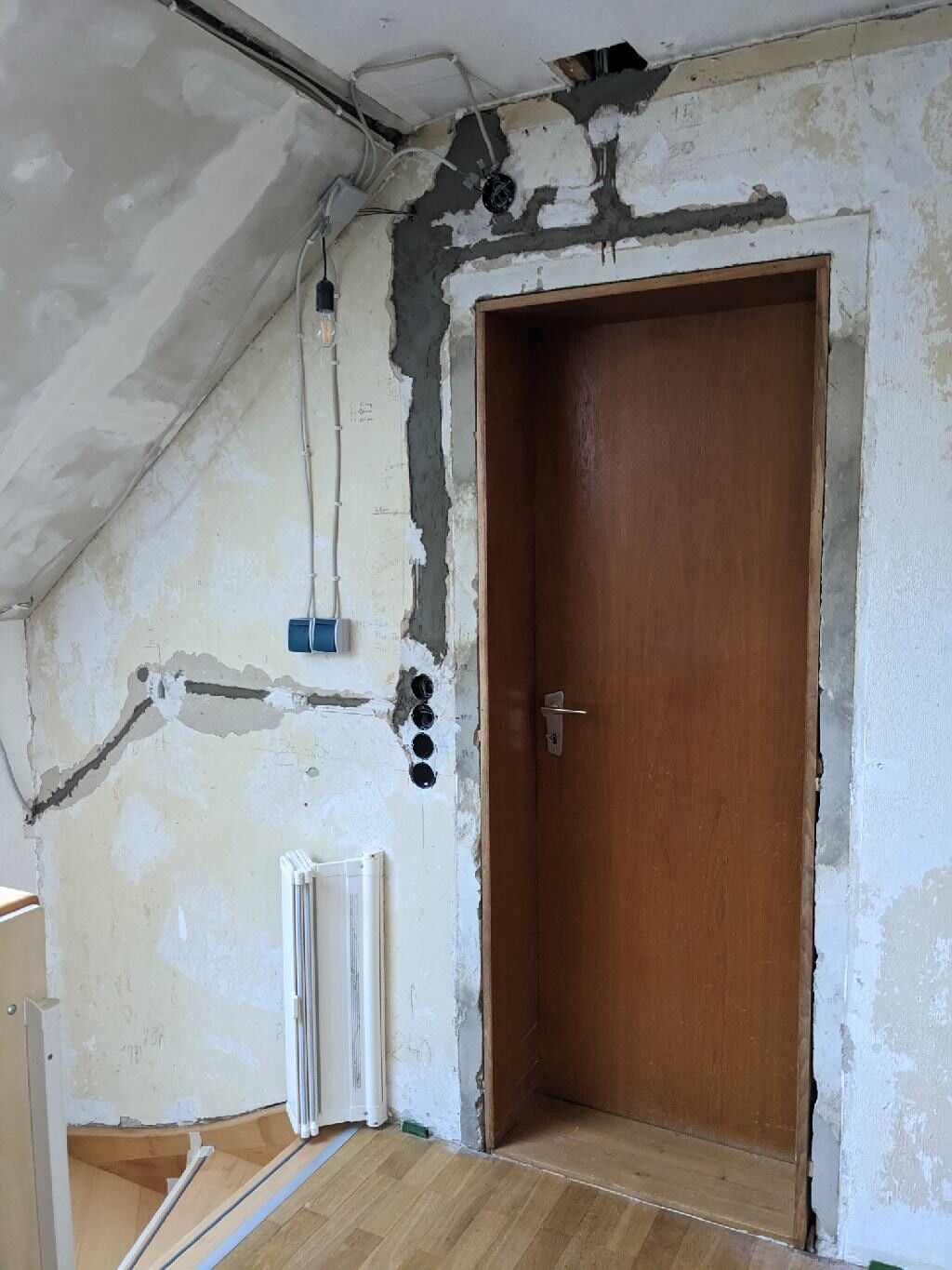 Renovierungsraum mit offener Holztür, roher Putz, Kabeln und Glühbirne