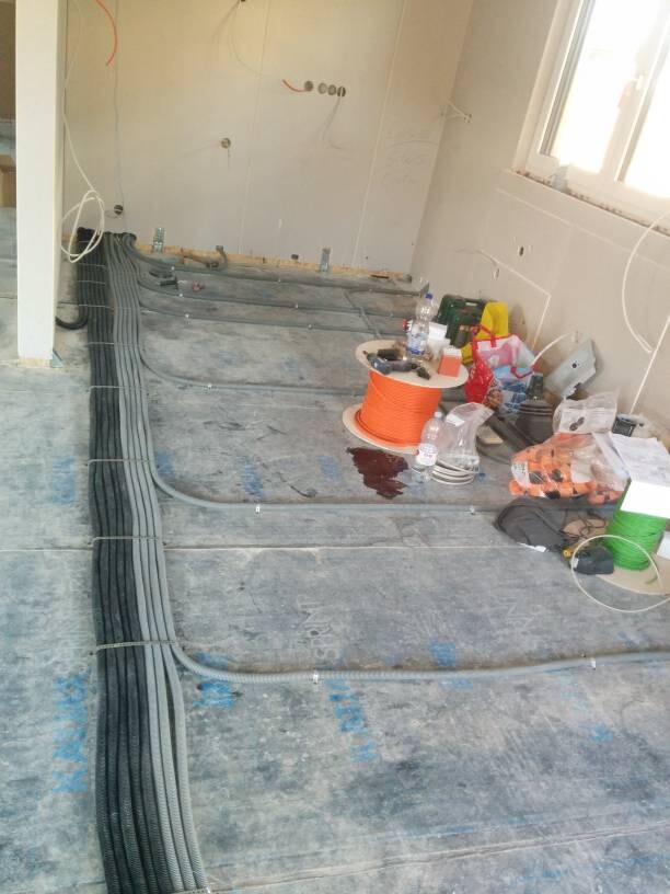 Baustelle: Kabelkanäle und eine orange Kabelrolle liegen auf dem Boden, Werkzeuge daneben.