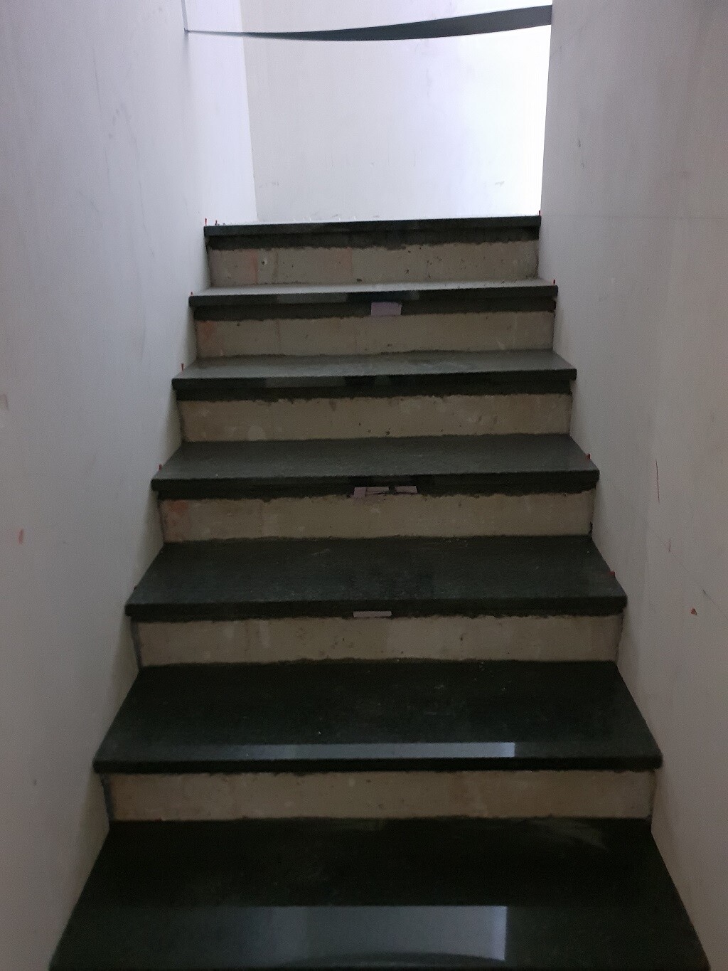 Innenstiege mit dunklen Stufen in hellem Treppenhaus, Licht am oberen Ende