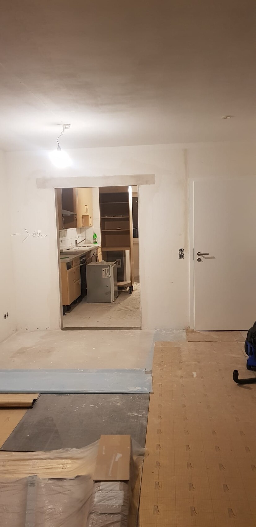 Unfertiger Innenraum mit offener Küchenzeile, Bau-Materialien, Bodenplatten und eine Glühbirne