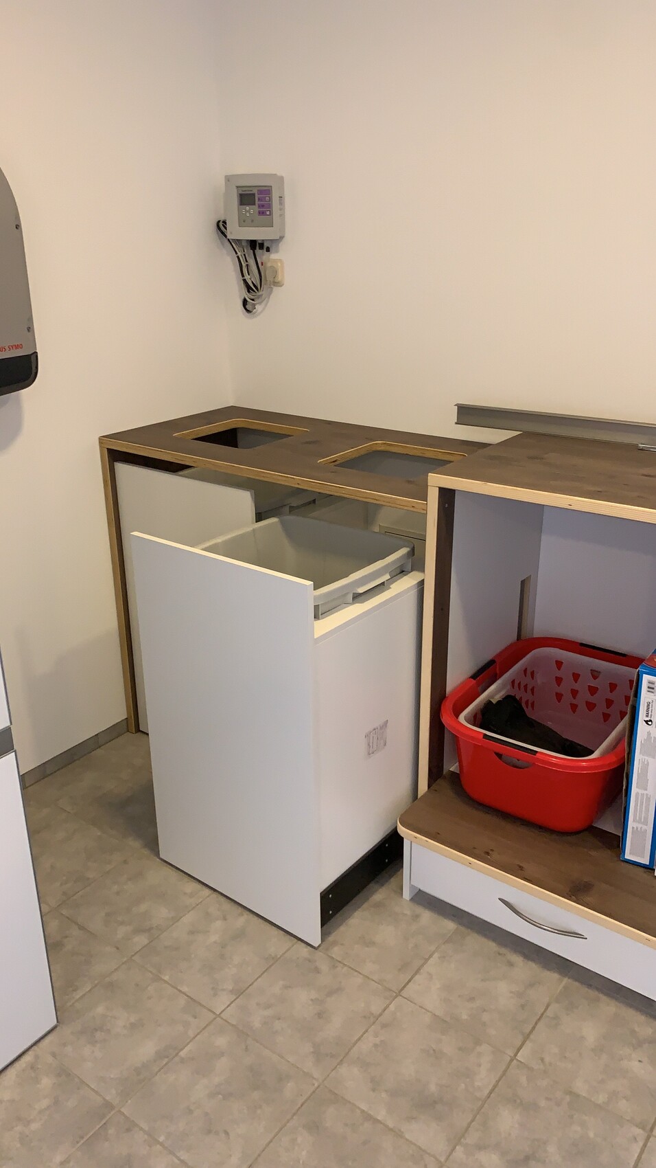 Kleiner Küchen-/Waschraum mit offener Schublade, Holz-Arbeitsplatte und rotem Wäschekorb.