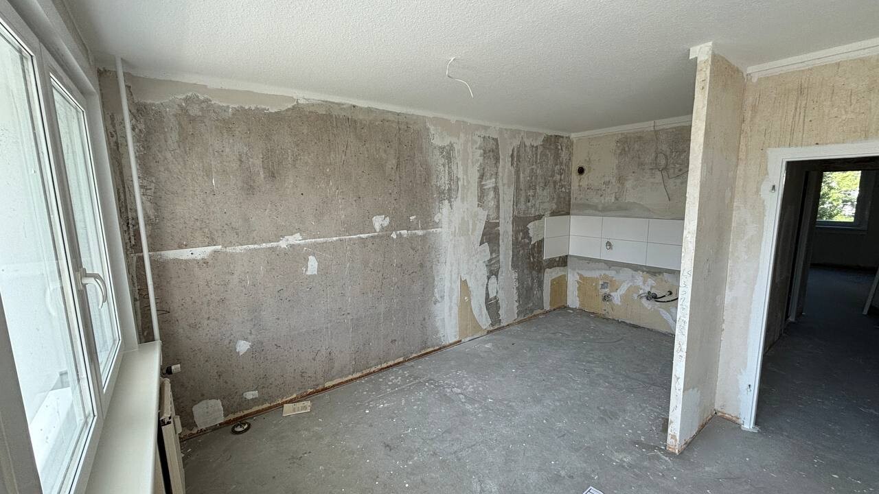Unrenovierte Küche: rohe Wände, teils Fliesen, Fenster links, Durchgang rechts.