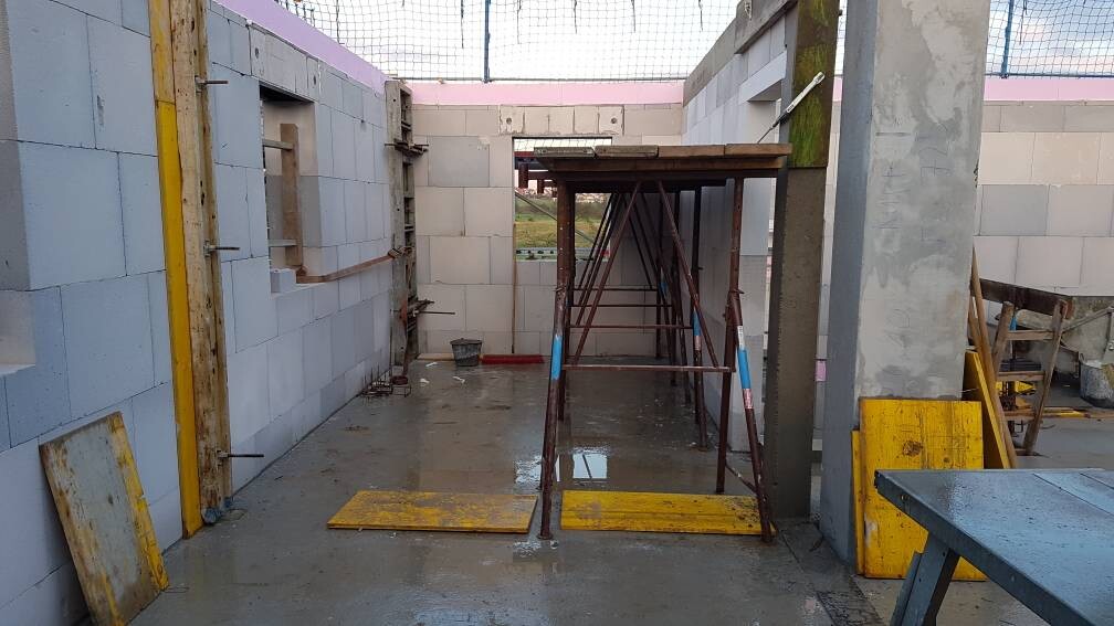 Baustelle: Unfertiger Innenraum mit Gerüst in der Mitte, weißen Blockwänden und nassem Boden.