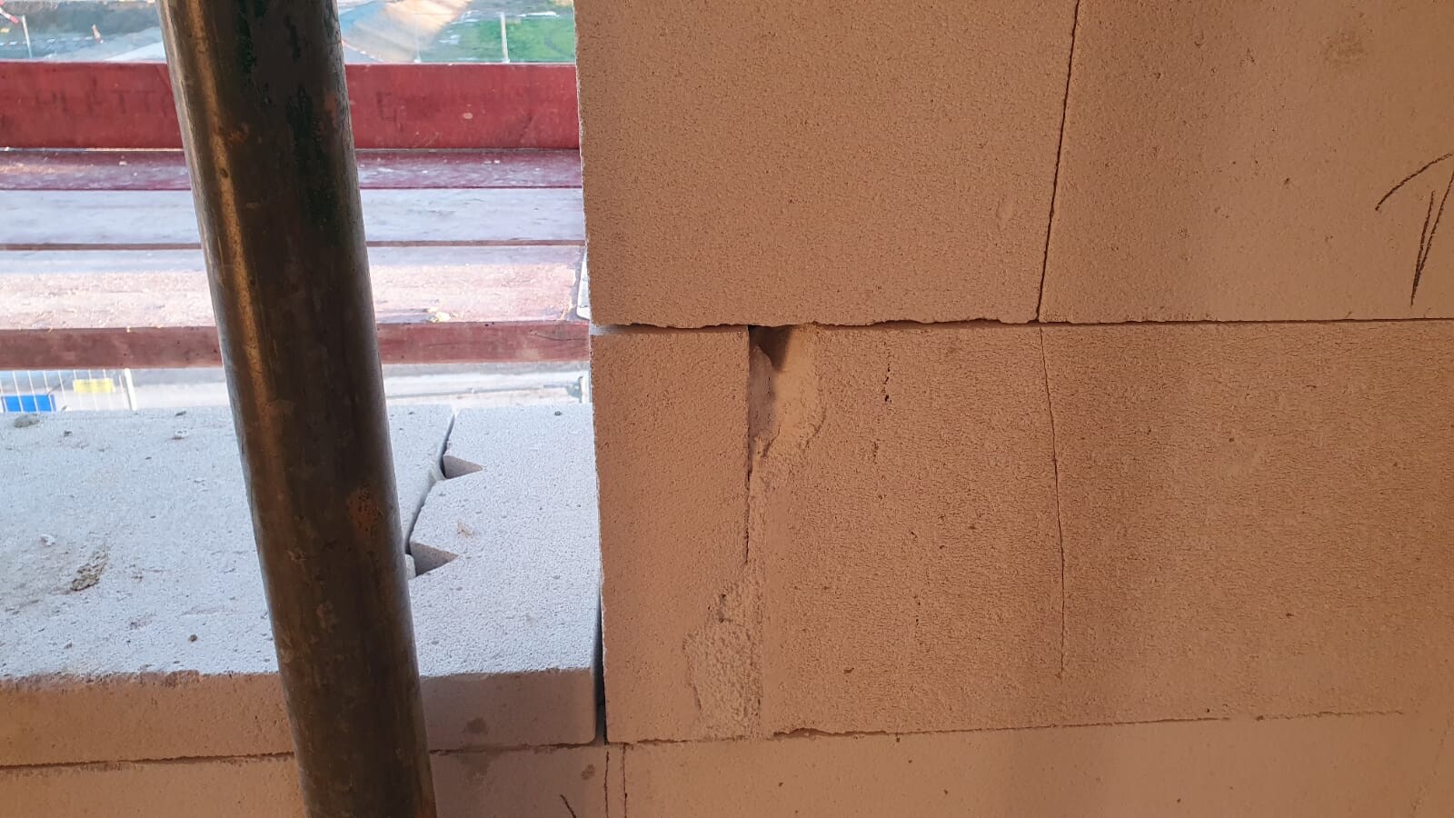 Baustellenszene: Stapel Porenbetonblöcke mit Rissen, links ein Metallrohr sichtbar.