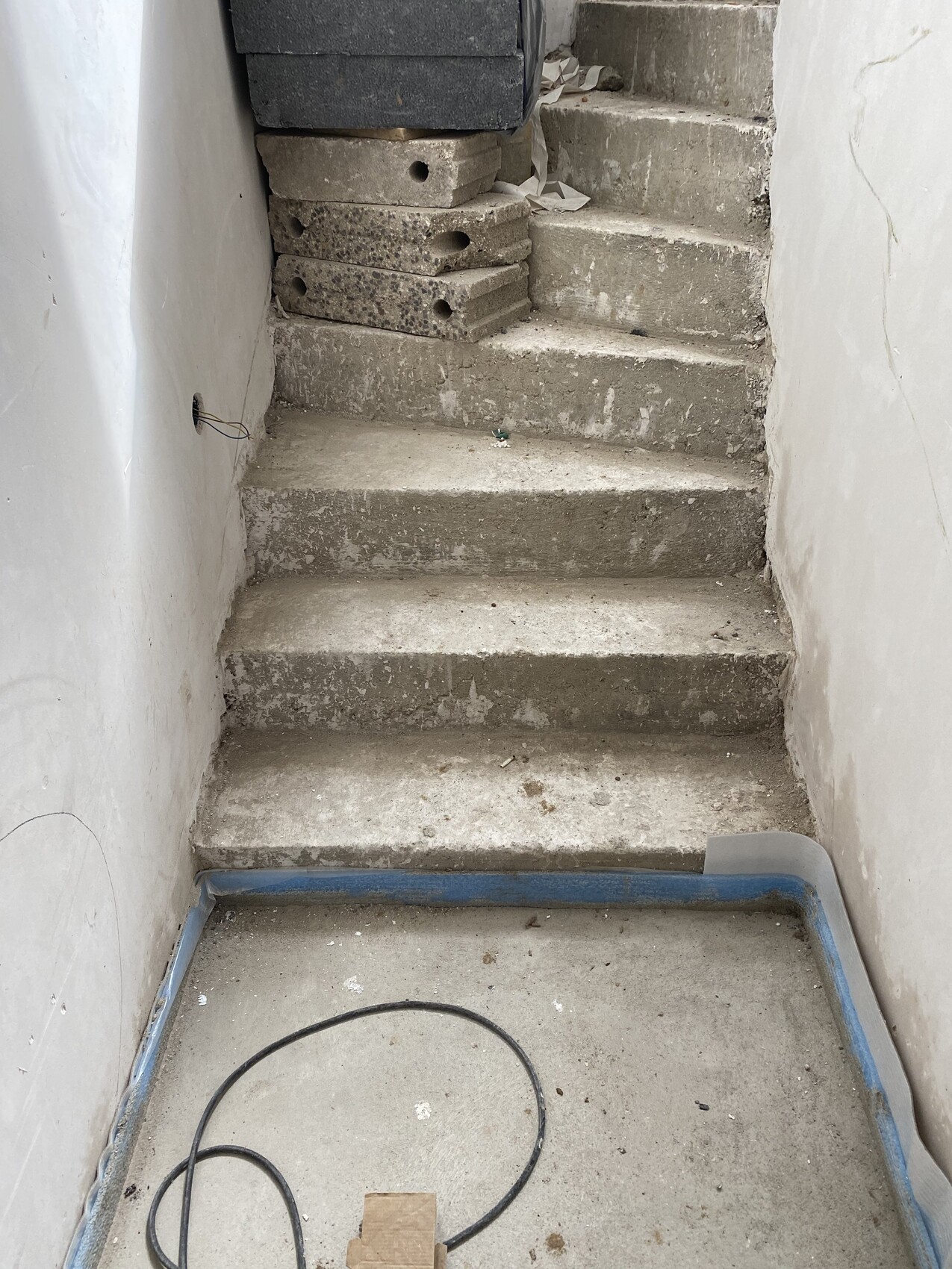 Unfertige Betonstufen mit gestapelten Blöcken oben und Kabeln auf dem Boden.