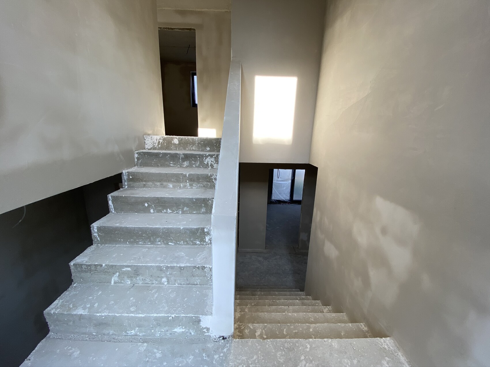 Rohbau-Treppenhaus mit Betonstufen, unfertigen Wänden und Lichtfenster.