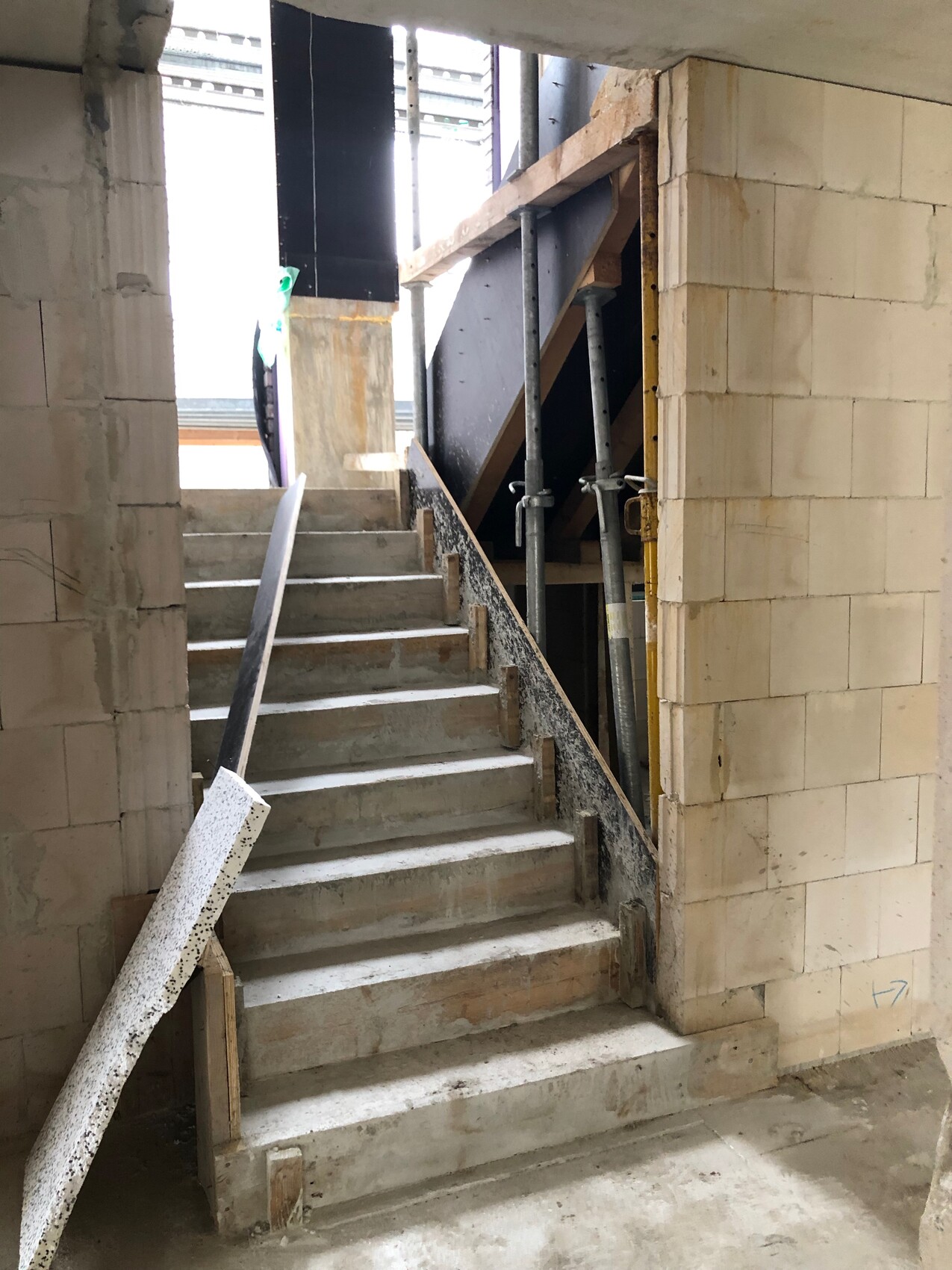 Innenbereich einer Baustelle: Sicht auf eine Betontreppe mit Geländer, Baugerüst und Wänden.