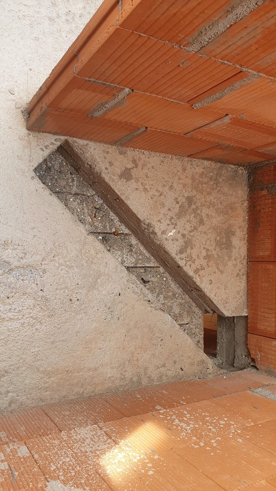 Baustelle mit rotem Ziegelmauerwerk, diagonal verlaufender Betontreppe und staubigem Boden.