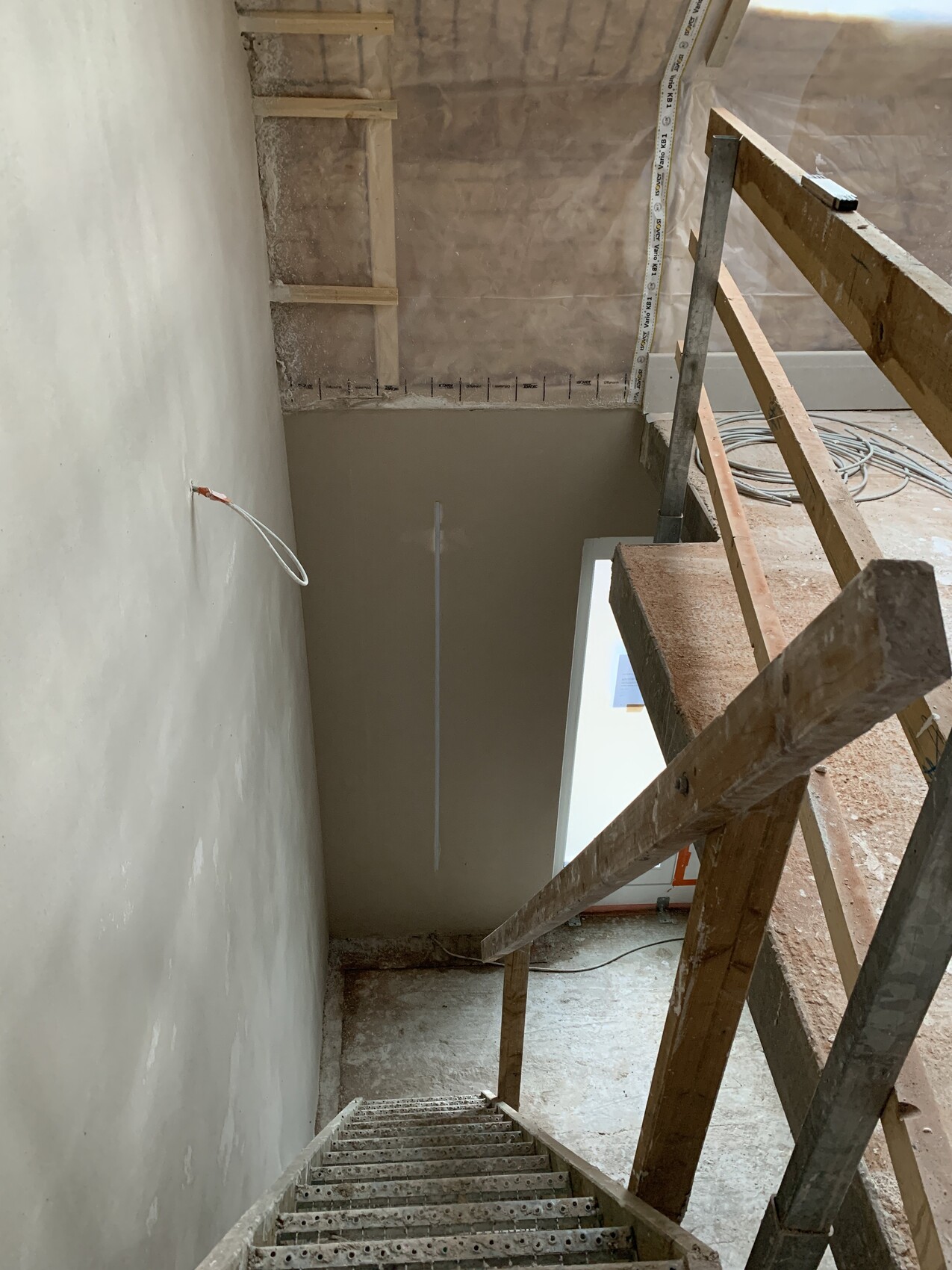 Baustelle innen: steile Treppe, Holzgerüst und Kabel an Wand, unfertige Verputzarbeiten.