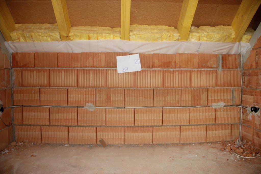Unfertige Ziegelwand in einer Bauhalle mit Dämmung an der Decke
